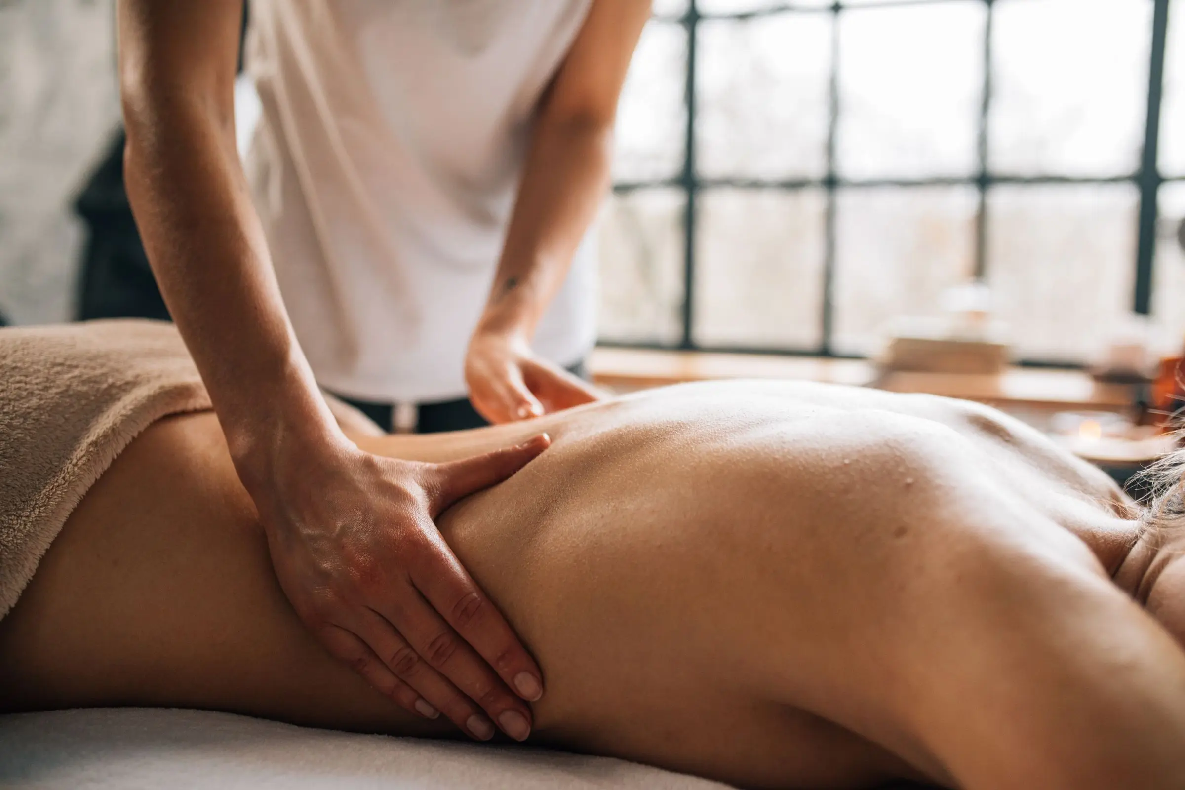 A massage therapist treating a client's back in a calm, warmly lit treatment room.