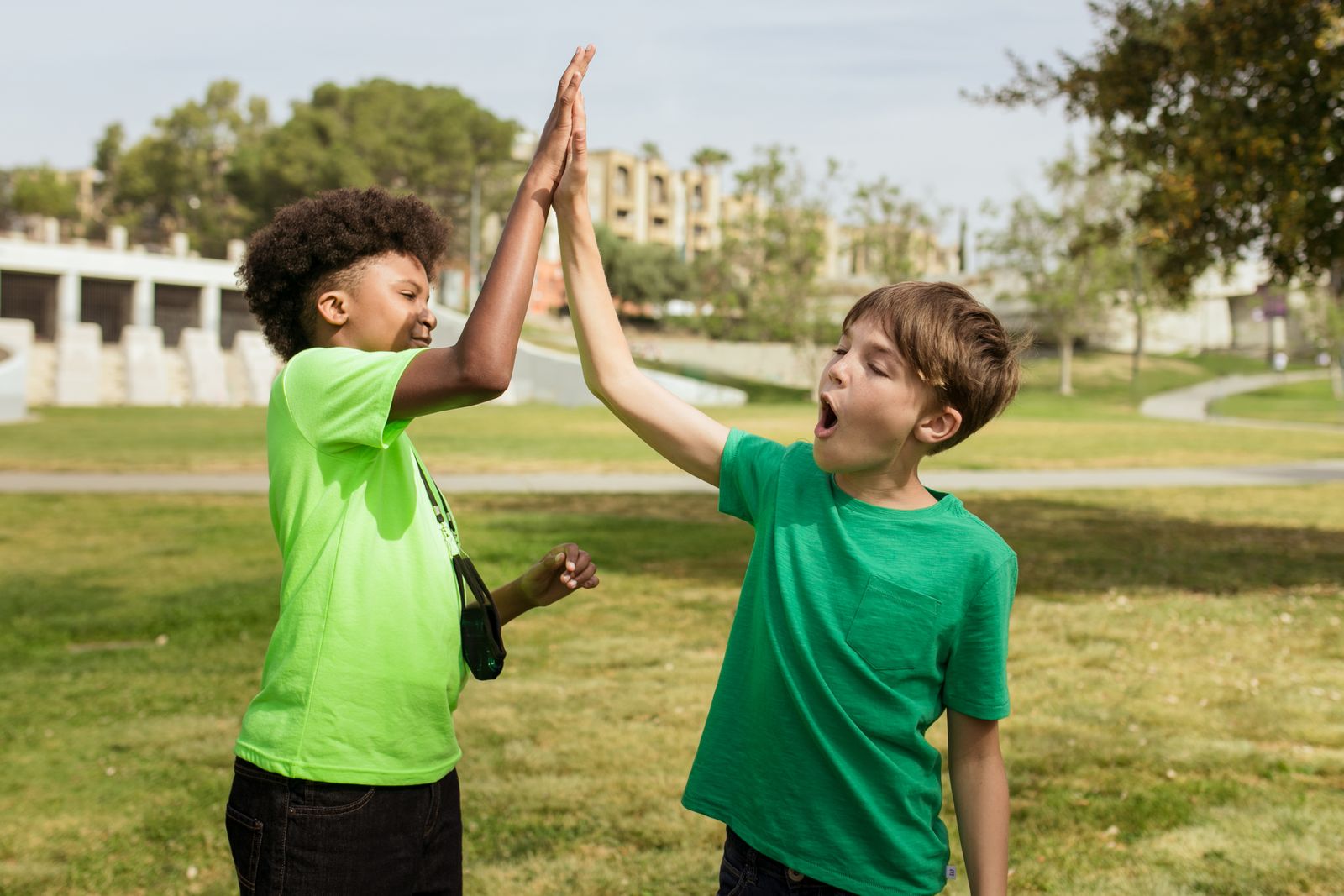 Two children high-fiving each other outside on a sunny day