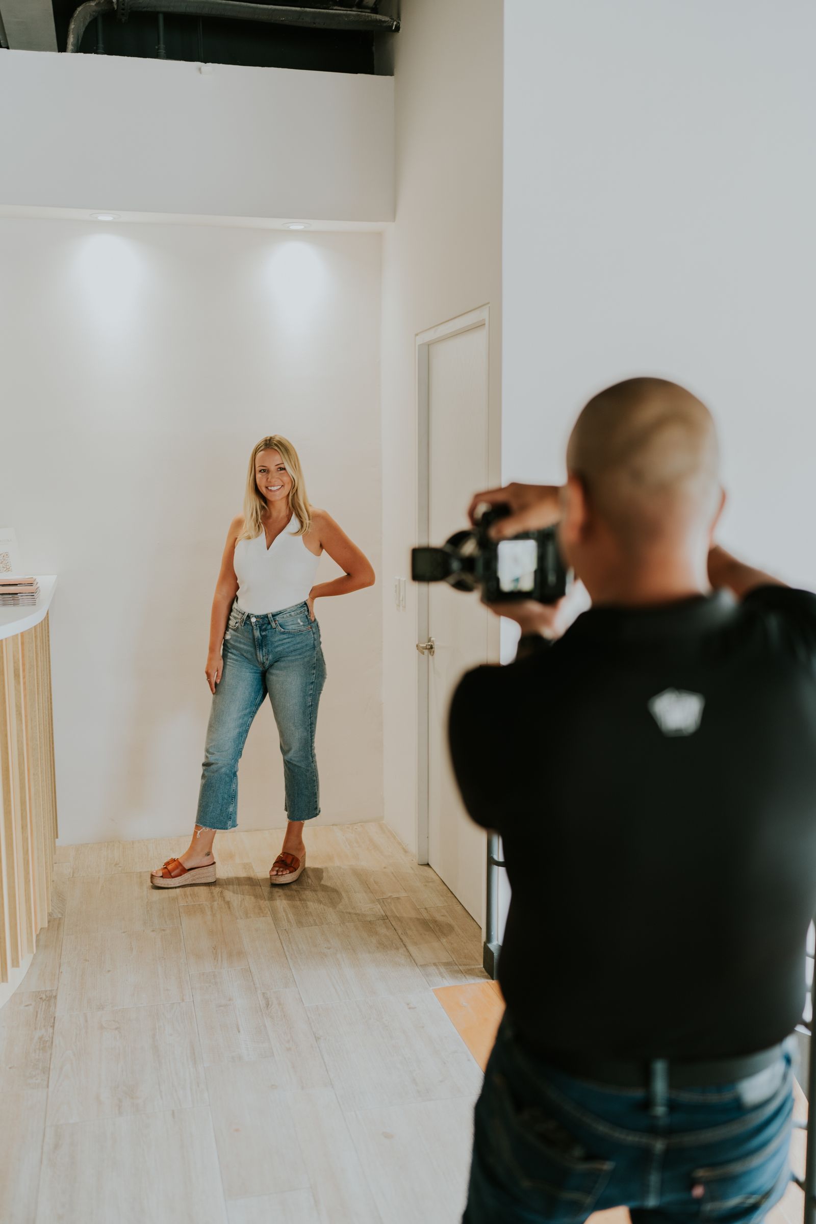 A photographer capturing a model posing in jeans in a bright white studio